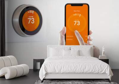 A person using a smart phone application warming up the room temperature with a wireless smart thermostat on a white background. Wall mural