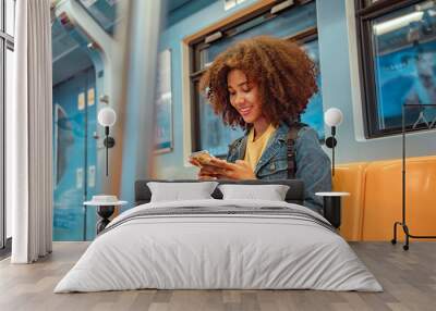 Happy young African American woman passenger smile and using smart mobile phone in subway train station. Wall mural