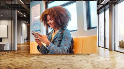 Happy young African American woman passenger smile and using smart mobile phone in subway train station. Wall mural