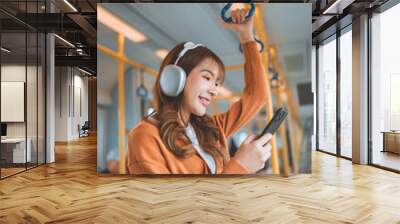 Happy young Asian woman passenger listening music via smart mobile phone in a train, Smile female wearing wireless headphones while moving in the tram, lifestyle, transportation. Wall mural