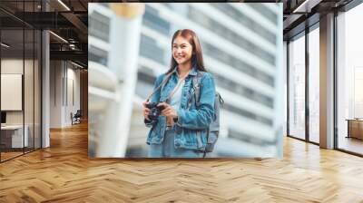 Happy young tourist asian woman holding a mirrorless camera on street in the city, Tourist journey trip concept Wall mural