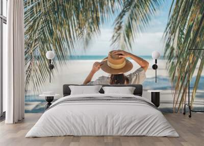 Summer beach vacation concept, Happy woman with hat relaxing at the seaside and looking away, in the summer against a backdrop of palm trees and sea beach. Wall mural