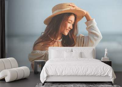 Summer beach vacation concept, Young asian woman with hat relaxing with her arms raised to her head enjoying looking view of beach ocean on hot summer day Wall mural