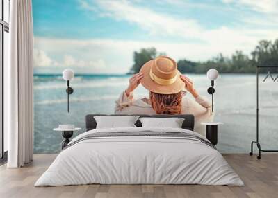 Summer beach vacation concept, Young woman with hat relaxing with her arms raised to her head enjoying looking view of beach ocean on hot summer day, copy space. Wall mural