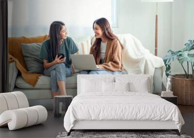 Two woman communicate with their friends and classmates via video link using a laptop and smartphone in the living room. Friends, friendship, time together Wall mural