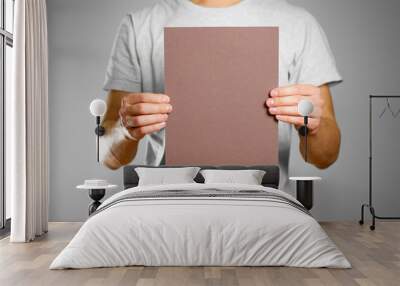 A man in a gray t-shirt keeps a brown clean blank sheet of A4. Isolated on grey background Wall mural