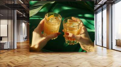 Close-up of female hands holding glasses with cocktails on green background Wall mural