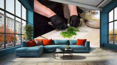 Chef's hands in black gloves chopping greens on board Wall mural