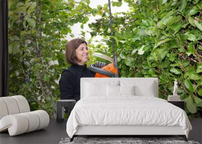 A woman trimming her hedge in the garden with a hedge trimmer Wall mural