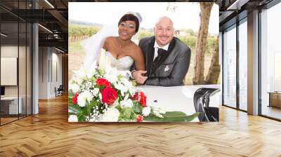 interracial american couple african bride posing on wedding car with caucasian groom Wall mural