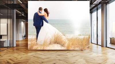 Look from behind at wedding couple walking along the sunny beach by rear view Wall mural