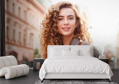 Portrait of cheerful young woman with curly hair in street city Wall mural