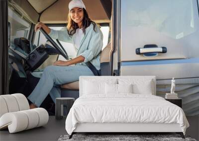 smiling female semi trailer truck driver sitting behind the steering wheel in jeans and cap Wall mural