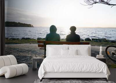 Two teenagers sitting on wooden bench evening beach Wall mural