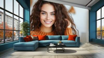 A bright and cheerful woman with voluminous curly hair smiles warmly while wearing a cozy sweater, capturing her vibrant personality and stylish appearance. Wall mural