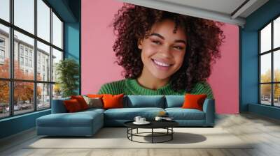 A cheerful, smiling young woman with curly hair stands against a vivid pink background, wearing a green sweater, exuding joy and a colorful modern aesthetic. Wall mural