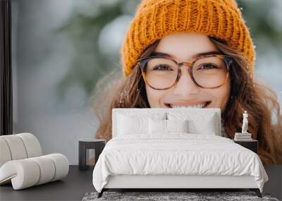 A cheerful woman wearing a mustard hat and glasses enjoys the snow in a cozy outdoor environment, emphasizing warmth and joy in the winter season. Wall mural