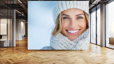 A close-up of a smiling blonde woman in white winter knitwear stands outdoors in a snowy setting, radiating warmth and contentment in a frosty atmosphere. Wall mural