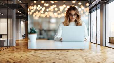 A woman wearing glasses works on a laptop in a modern office environment, surrounded by decorative hanging lights creating a professional ambiance. Wall mural