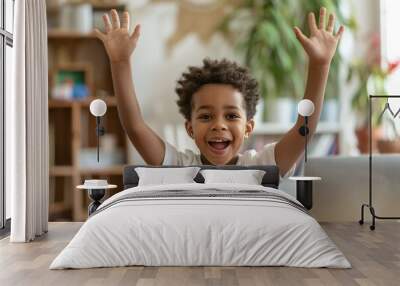 A young child exuberantly raises their hands with a big smile, expressing pure joy and happiness while being inside a comfortable and cozy home environment. Wall mural