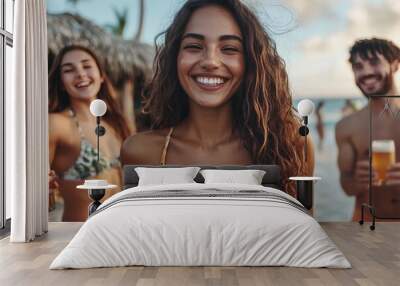 A young woman in a floral bikini is having a great time at the beach, smiling at the camera with friends in the background, enjoying drinks and a sunny, tropical vibe. Wall mural