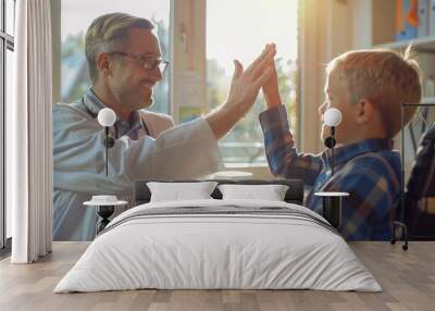 In a warmly lit doctor's office, a friendly male doctor shares a high-five with a young boy, fostering a sense of comfort and trust in the healthcare environment. Wall mural