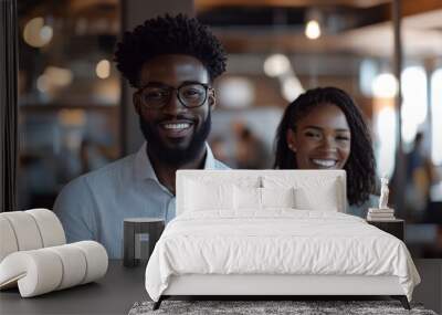 Two happy coworkers candidly smile while holding tablets in a lively, open-plan office space, highlighting teamwork, camaraderie, and a collaborative work culture. Wall mural