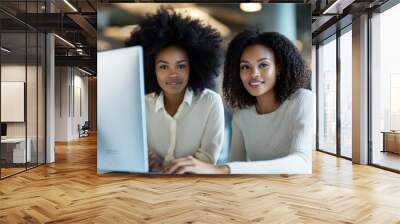 Two women, focused and engaged, collaborate in a modern office environment. Their teamwork and synergy are evident as they work on a project using the computer. Wall mural