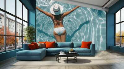 Woman in a bikini and sun hat floating in a clear blue pool on a sunny day Wall mural