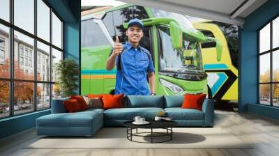 A bus driver in uniform and hat smiles with a thumbs up against the background of the bus Wall mural