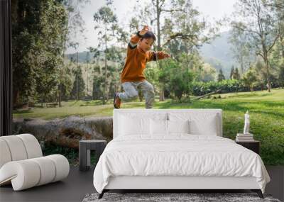 A joyful child leaps over a log in a vibrant outdoor scene filled with lush greenery Wall mural