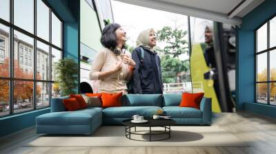 a woman in a veil with a bag looks at the bus door while chatting and laughs with a female friend while getting on the bus Wall mural