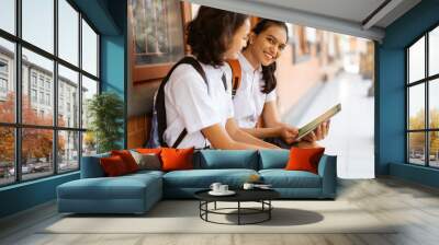 Asian high school student smiling while using a pad while sitting outside the classroom Wall mural