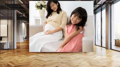 Asian little girl smiling when sit on sofa with mother pregnant background Wall mural