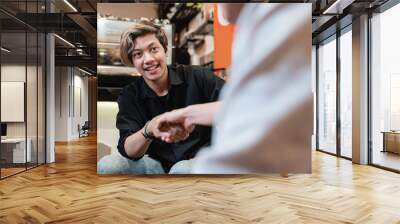 asian young man shake hands with partner when sitting on sofa in coffee shop Wall mural