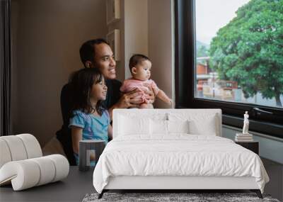 father and two little daughter seeing out of the window glass when sitting on the bed in bedroom Wall mural