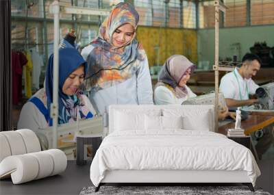 female supervisor stands to the side and sees the seamstress using the sewing machine in the production room Wall mural