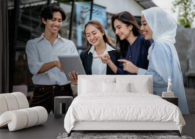 Group of cheerful young businesspeople using a tablet work together on a new project while standing at an outdoor workplace Wall mural