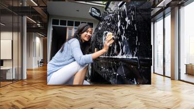 happy asian woman cleaning and washing her black car by herself in the carpot of her house Wall mural