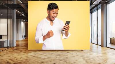 happy asian young man looking at the screen of a mobile phone on isolated background Wall mural