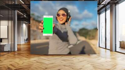 hijab woman wearing sportswear holding green screen phone for mockup Wall mural