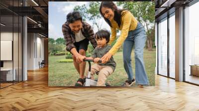 little boy learning to ride a bike with mom and dad outdoors Wall mural