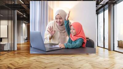 mother and her daughter wave her hand to laptop computer during class meeting with school from home Wall mural