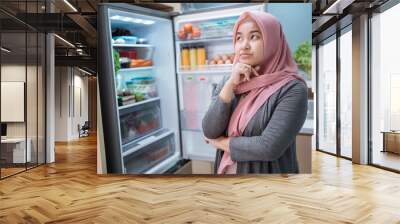 muslim asian woman thinking while open the refrigerator door before cooking in the kitchen Wall mural