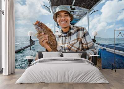 smiling Asian angler holding a grouper on a small fishing boat Wall mural