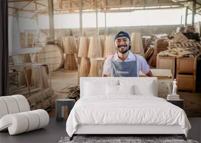 smiling Asian male entrepreneur standing wearing an apron in a woodcraft warehouse Wall mural