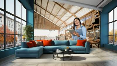 smiling female entrepreneur wearing an apron works with a digital tablet in a wood processing workshop Wall mural