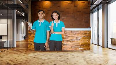 two janitors wearing turquoise uniforms smiling while standing with thumbs up in hotel lobby Wall mural