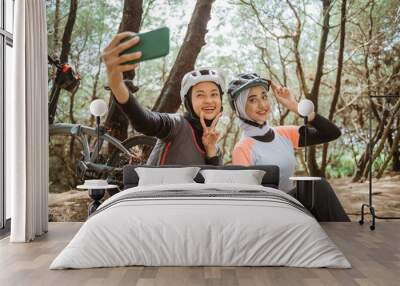 two veiled girls selfie with v sign using cellphone while cycling in park Wall mural