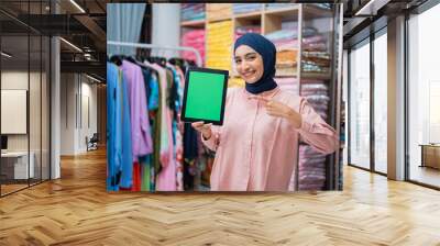 woman with hijab showing her blank screen to camera while working at her fashion warehouse. online seller Wall mural